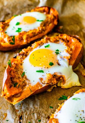 Close up side view of multiple breakfast twice baked sweet potatoes on a baking sheet, garnished with salt, pepper, and parsley.