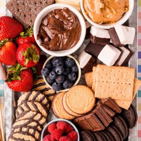 Decked out s'mores charcuterie board with graham crackers, chocolate, marshmallows, fruit, and cookies.