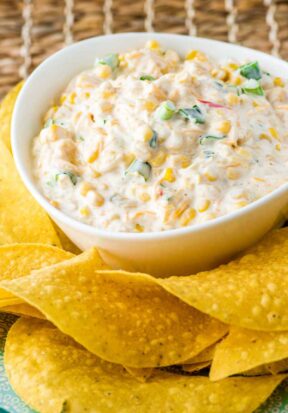 Prepared corn dip in a white bowl surrounded by tortilla chips.