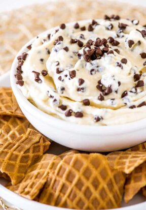 Close up side view of a bowl of cannoli dip on a plate surrounded by broken waffle cones.