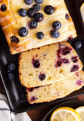 Top down view of blueberry lemon cream cheese loaf on a dark serving plate, half of the loaf is cut with the cut slices laying facing up toward the camera.