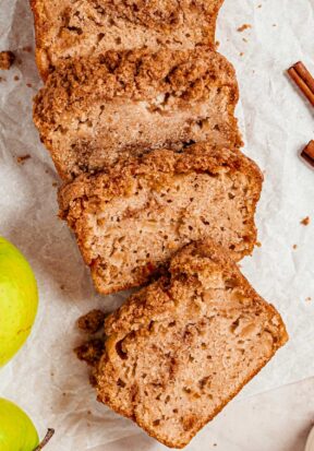 Top down view of multiple slices of apple streusel bread, laying against each other in an elongated pattern, surrounded by whole green apples.