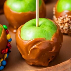 Side view of multiple homemade caramel apples resting on a wooden tray.