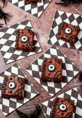 Top down view of multiple Hocus Pocus book brownies resting on black and white checkered napkins, on a table coated in spiderwebs.