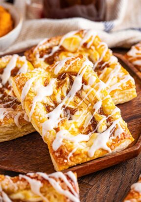 Side view of multiple prepared and glazed pumpkin cream cheese danish, with the closest danish stacked at an angle, showing off the pumpkin swirl and glaze.