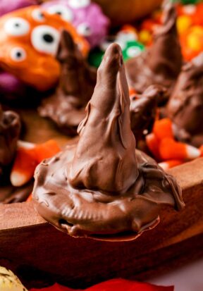 Close up side view of a decorated sorting hat cookie, sitting on the edge of a wooden tray, surrounded by colorful candies and more decorated sorting hats.