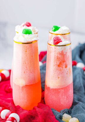 Side view of four tall, thin glasses filled with gumdrop punch, each garnished with whipped cream and topped with a gumdrop.