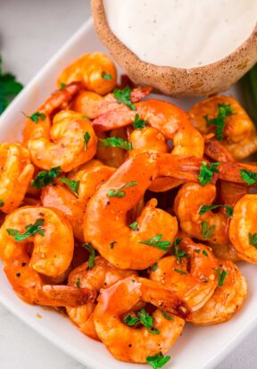 Close up side view of a plate piled high with prepared buffalo shrimp, served with a large bowl of ranch.