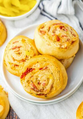 Top down view of three baked Italian crescent roll pinwheel on a white decorative plate.