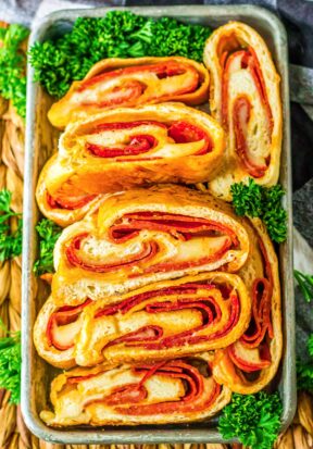 Top down view of a tray filled with slices of pepperoni bread, surrounded by parsley garnish, pictured with the slices facing up, showing off the ingredients inside.