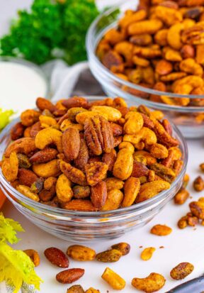 Side view of multiple bowls filled with buffalo ranch roasted nuts, pictured with more roasted nuts scattered about, with fresh celery and carrots nearby.