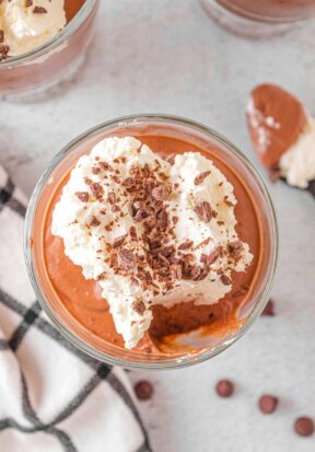 Top down view of a glass serving cup filled with chocolate mousse, topped with whipped cream and chocolate shavings.