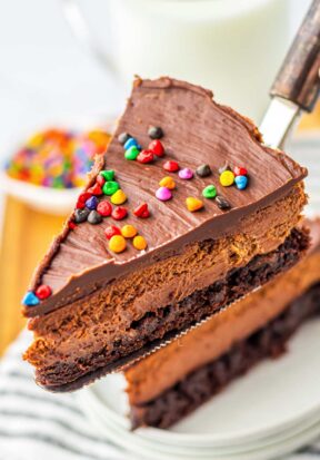 Close up side view of a cake spatula holding a freshly cut slice of cosmic brownie cheesecake up to the camera.