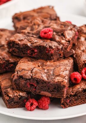 Close up side view of a pile of raspberry brownies on a plate, showing off the pieces of raspberries baked inside each square.