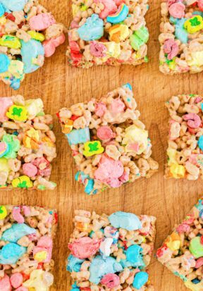 Top down view of multiple Lucky Charms cereal bars arranged in rows on a cutting board.