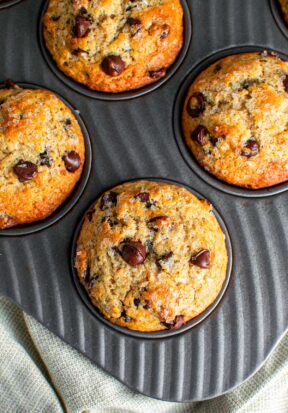 Top down view of multiple chocolate chip muffins, resting in a muffin tin.